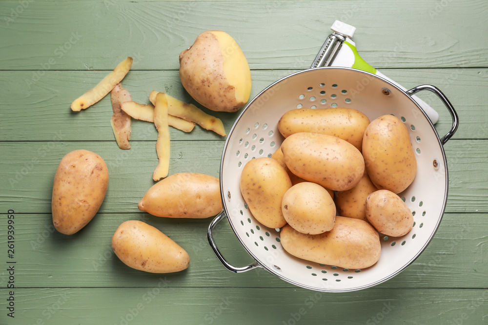 Colander with raw potatoes on wooden table