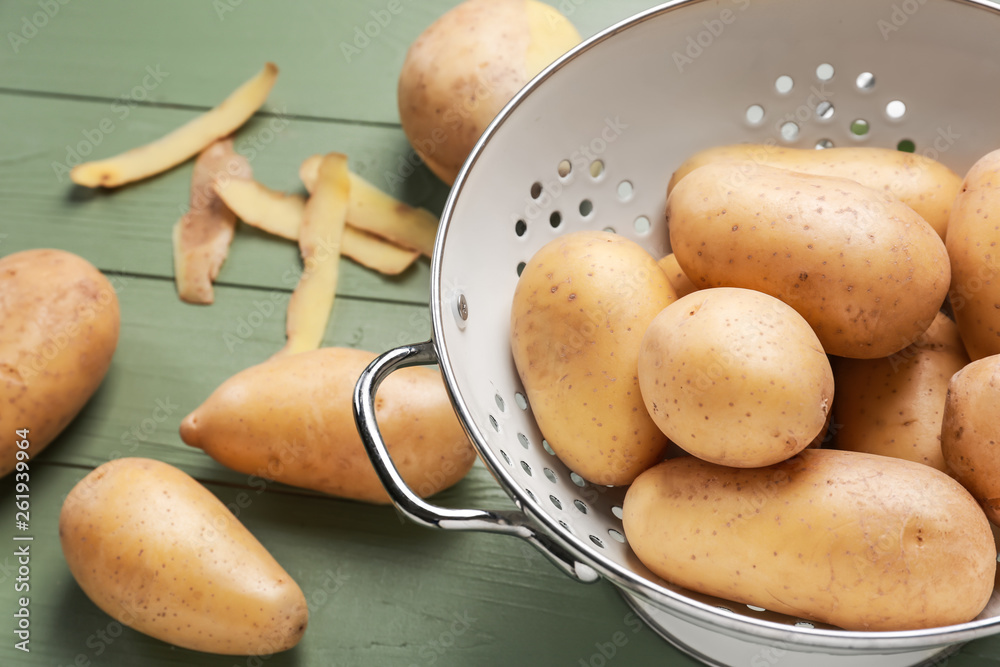 Colander with raw potatoes on wooden table