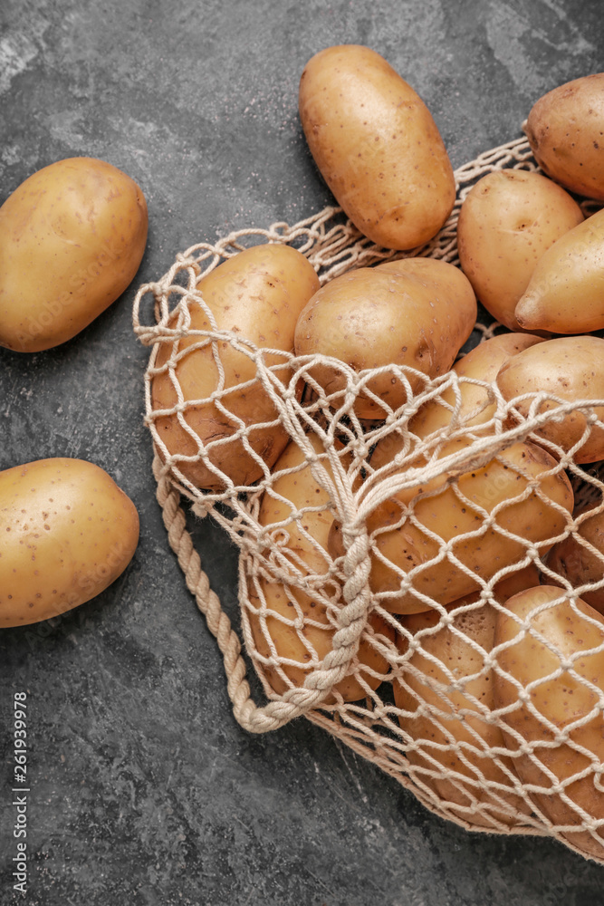 String bag with raw potatoes on grey background