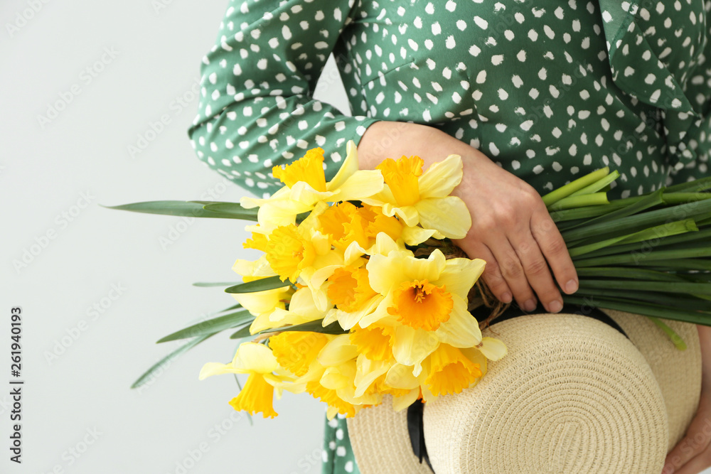 Woman with bouquet of beautiful daffodils on light background, closeup