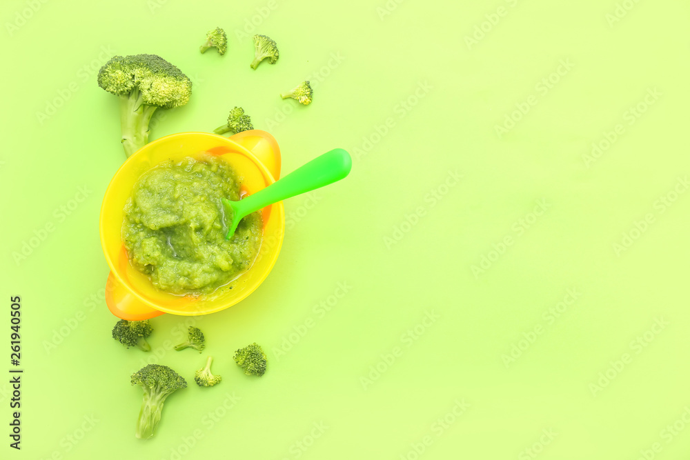 Bowl with healthy baby food on color background