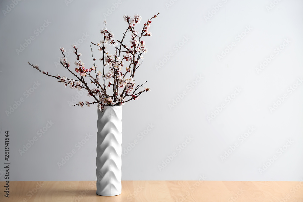 Vase with beautiful blossoming branches on table against light background