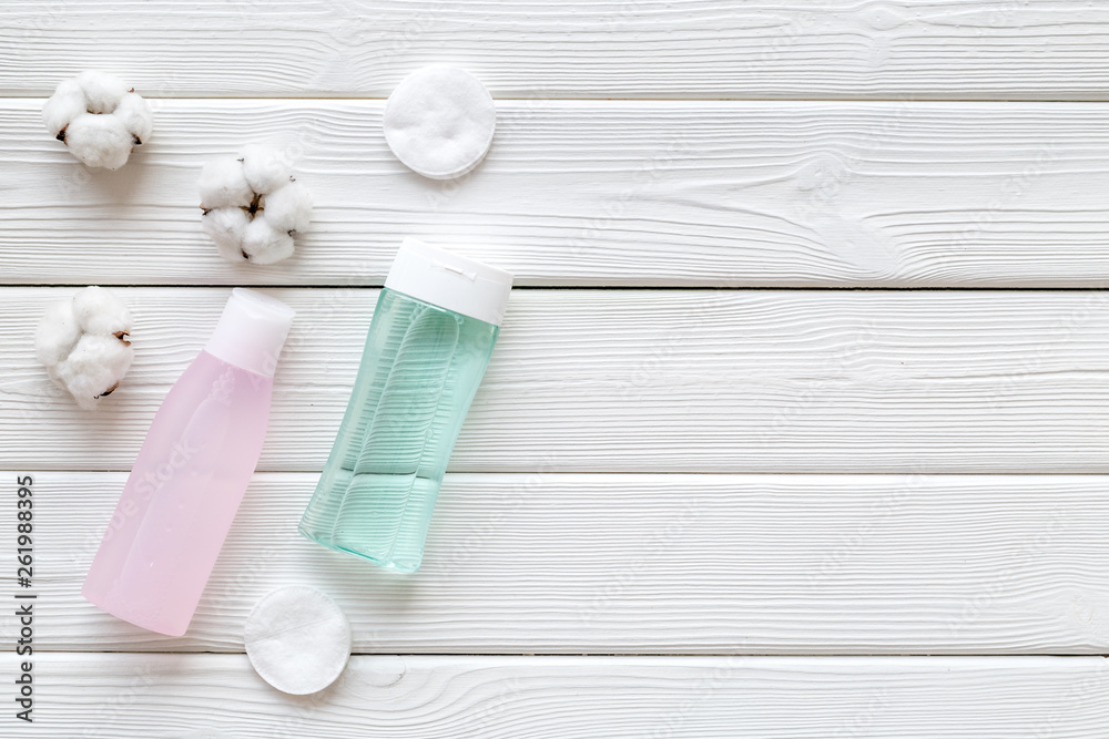 facial tonic, lotion and cotton pads for face care on white wooden background top view mock up