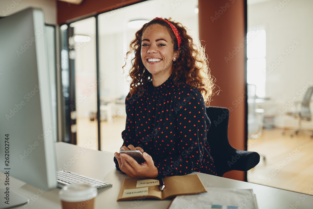 Smiling young businesswoman using a cellphone at her office desk