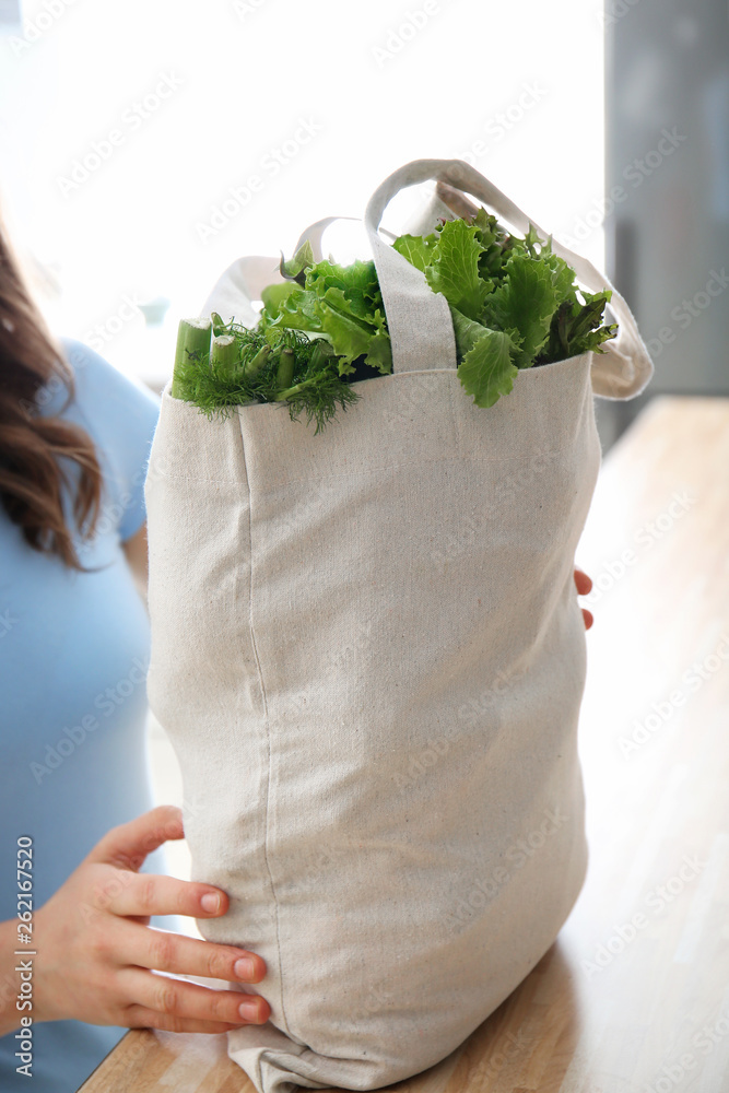 Young woman with fresh vegetables in eco bag indoors