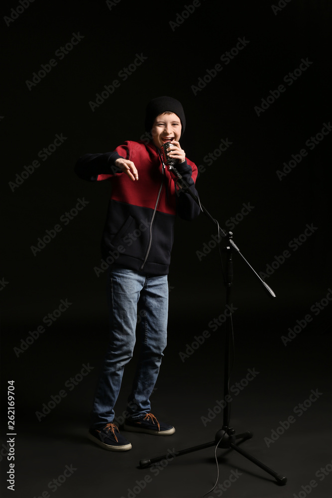 Teenage boy with microphone singing against dark background