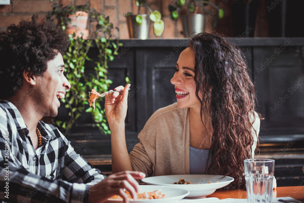 Happy young couple eating lunch together at restaurant, african american people having fun