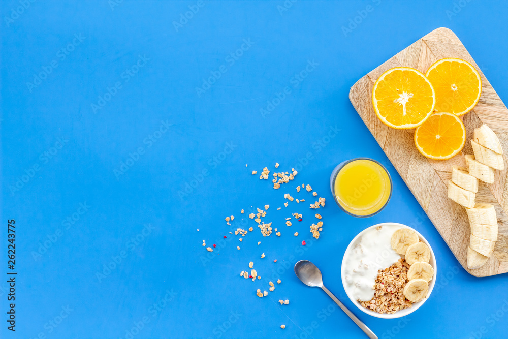 Healthy granola with banana and orange juice for colorful breakfast on blue background top view mock