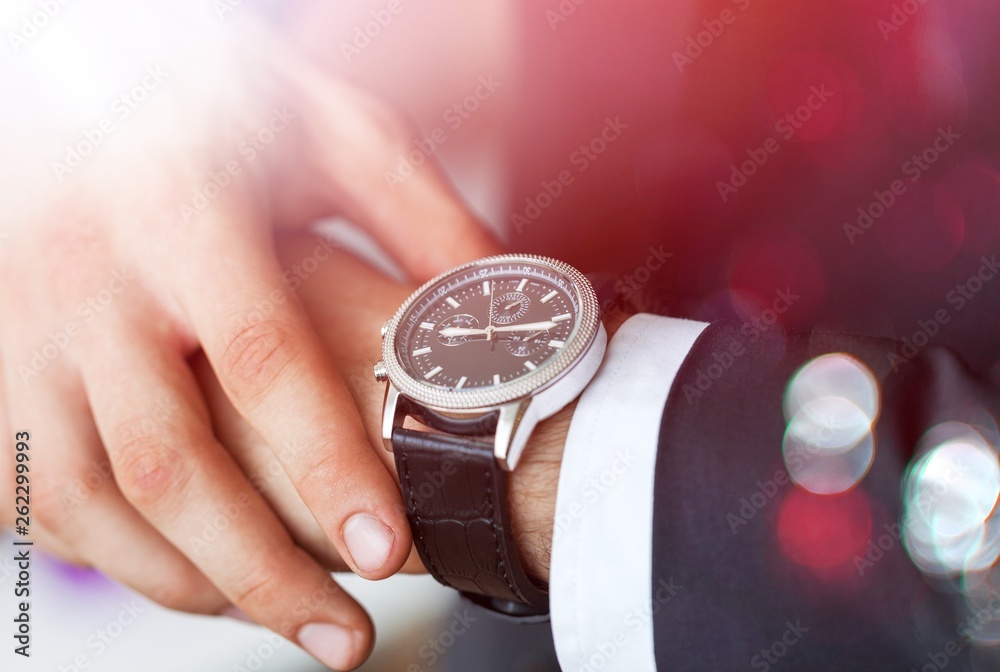 Businessman pointing at hand watch on grey wall background, close-up