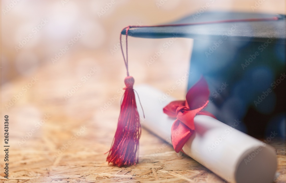 Graduation hat and diploma on wooden background