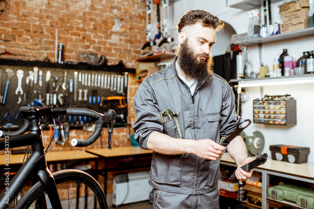 Handsome bearded repairman in workwear serving a sports bike at the bicycle workshop