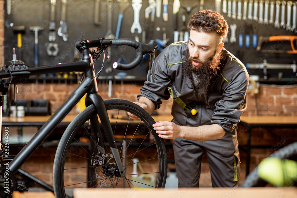 Handsome bearded repairman in workwear serving a sports bike at the bicycle workshop