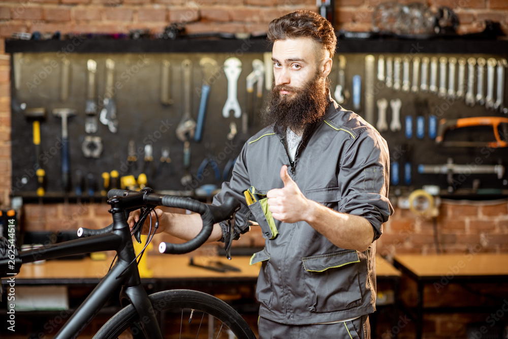 Portrait of a handsome bearded repairman in workwear at the bicycle workshop