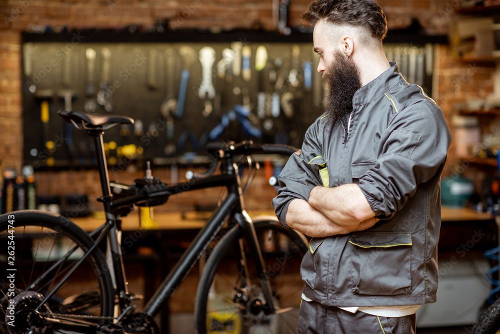 Portrait of a handsome bearded repairman in workwear at the bicycle workshop