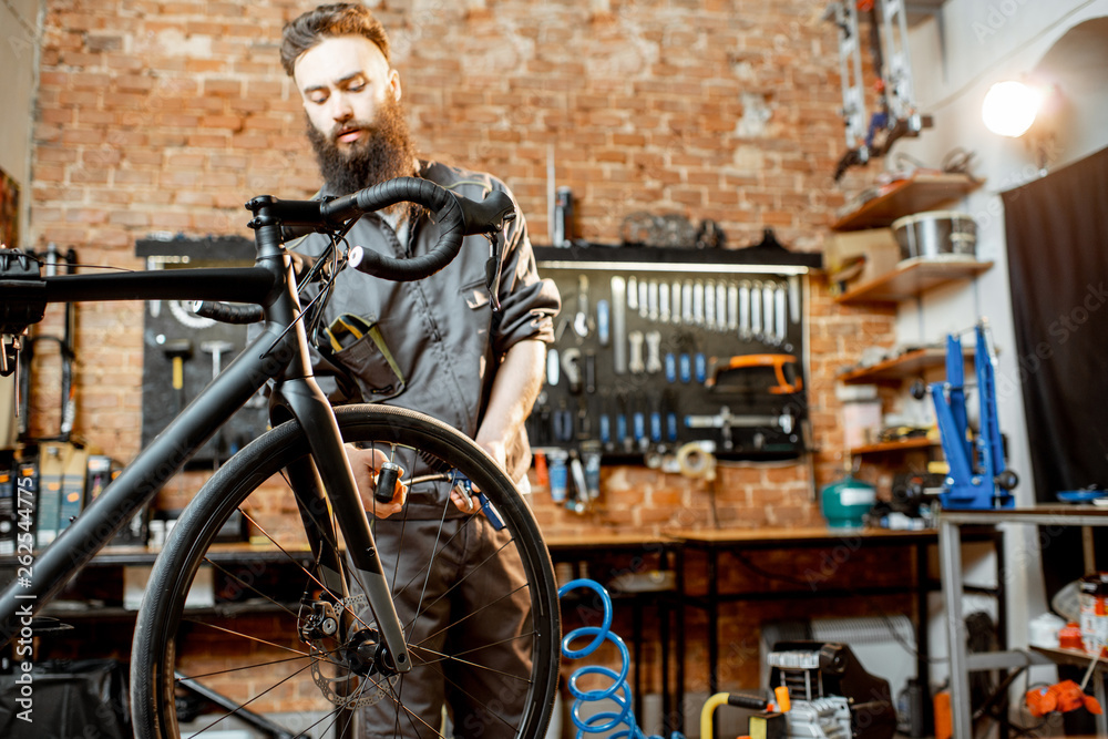 Handsome bearded repairman in workwear serving a sports bike at the bicycle workshop