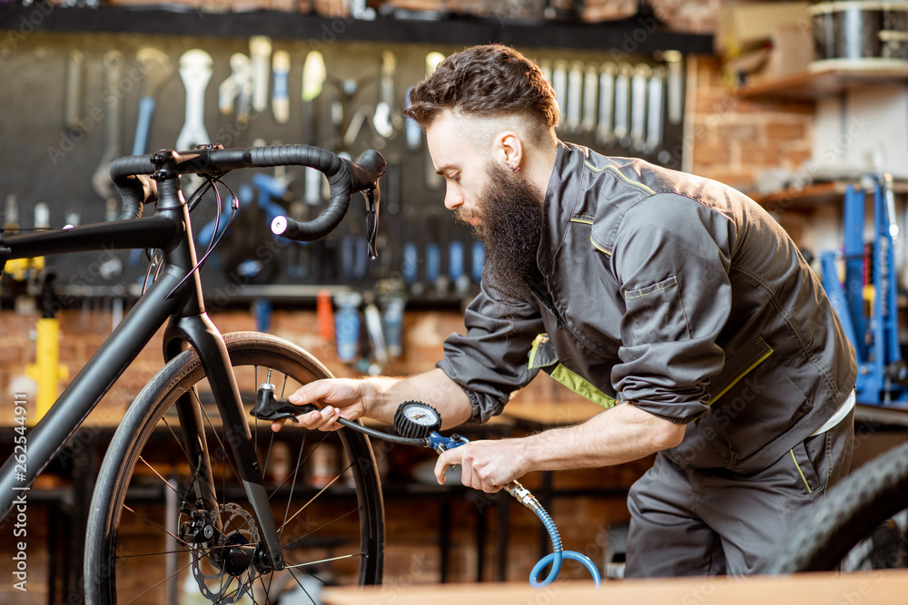 Repairman in workwear serving a sports bike, pumping wheels at the bicycle workshop