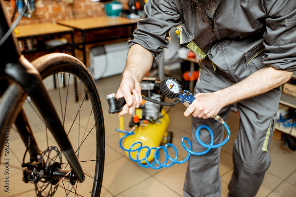 Repairman in workwear serving a sports bike, pumping wheels at the bicycle workshop