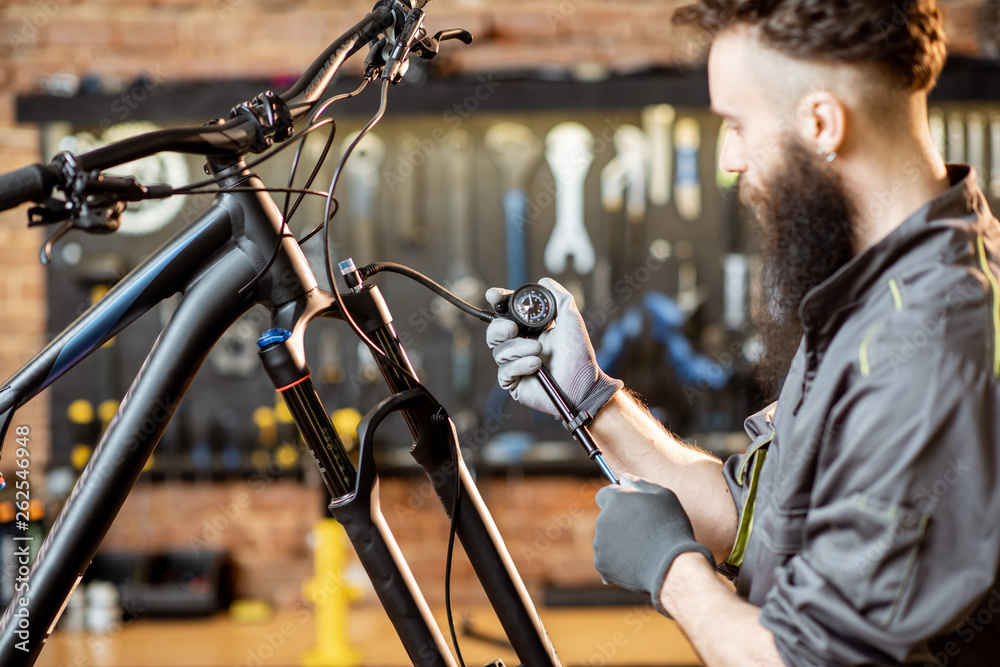 Repairman pumping shock absorber of the mountain bike in the workshop of the bicycle shop