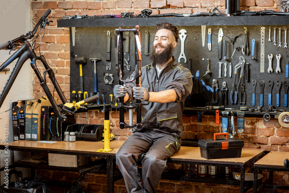 Portrait of a handsome repairman in workwear sitting with bicycle fork on the table in the bicycle w