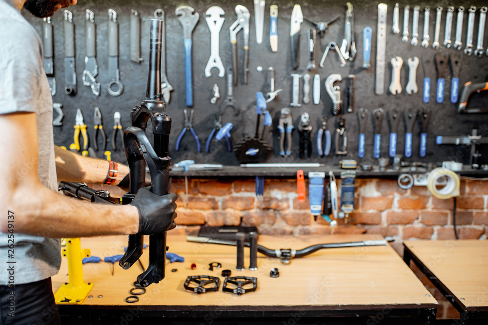 Man disassembling shock absorber of a bicycle fork at the workshop, close-up view