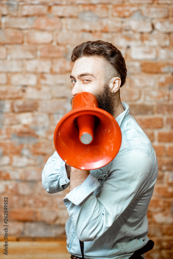 Handsome bearded man with red loudspeaker on the brick wall background