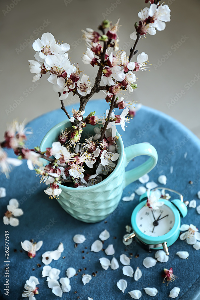 Cup with beautiful blossoming branches and alarm clock on table