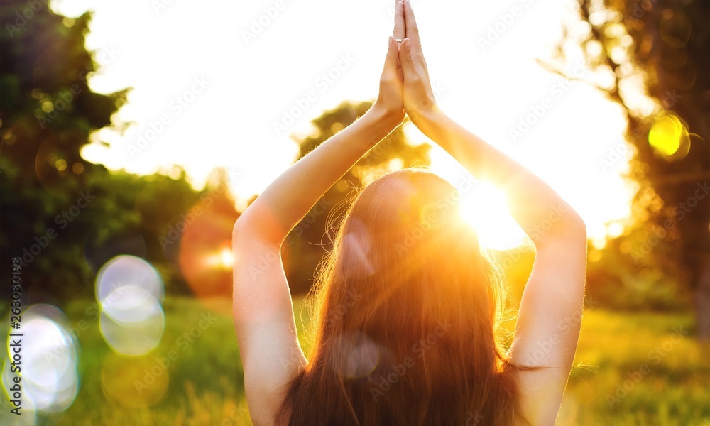 Young woman on field under sunset light doing yoga