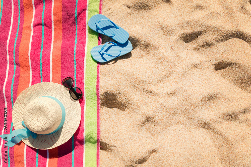 Beach towel with hat, sun glasses and flip flops on sand