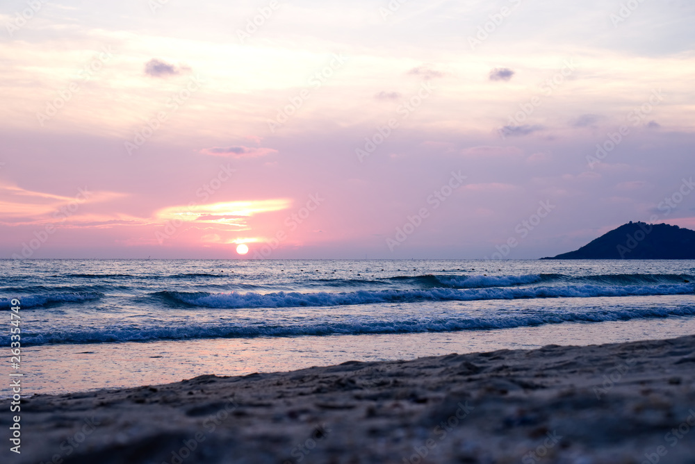 Colorful ocean beach sunset with deep orange blue sky and sun rays. Foreground is sand at the beach 