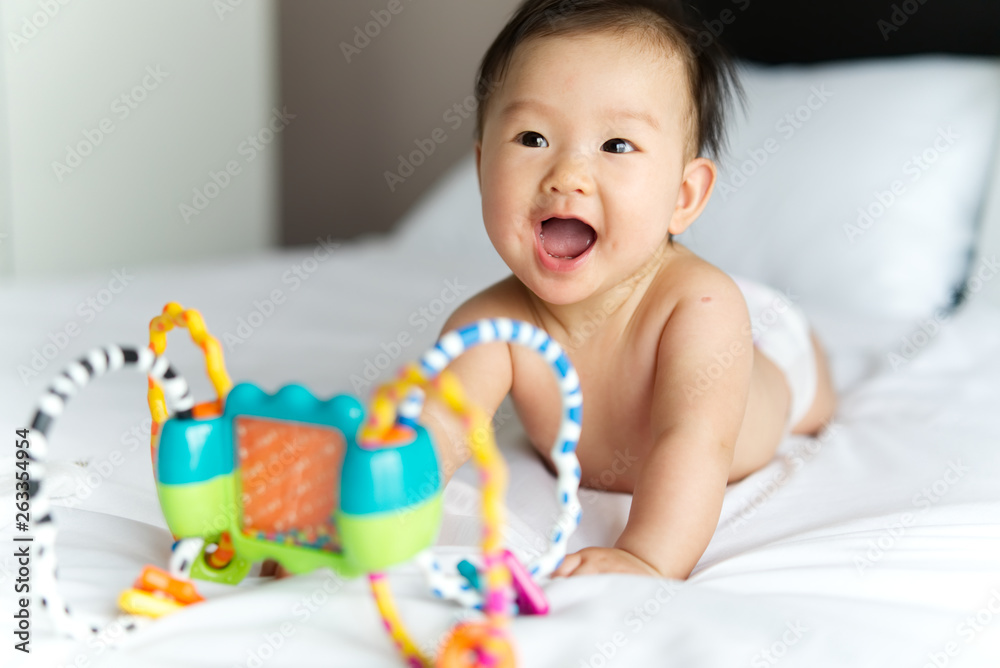 Asian cute baby crawling and playing toy on bed at home. Baby is smiling and feeling happy with it. 