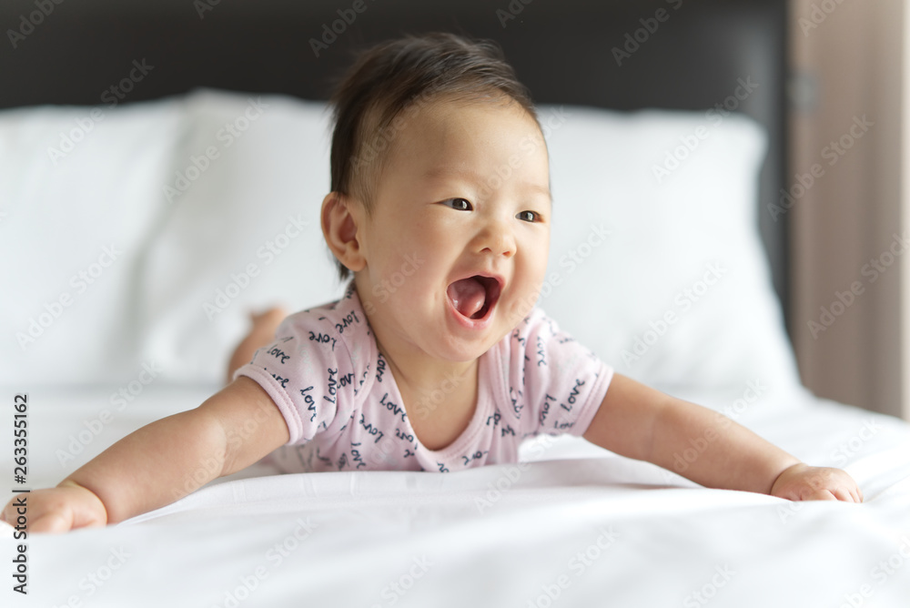 Young cute Asian baby crawling and spreading arms on bed in bedroom. The baby is smiling and playing