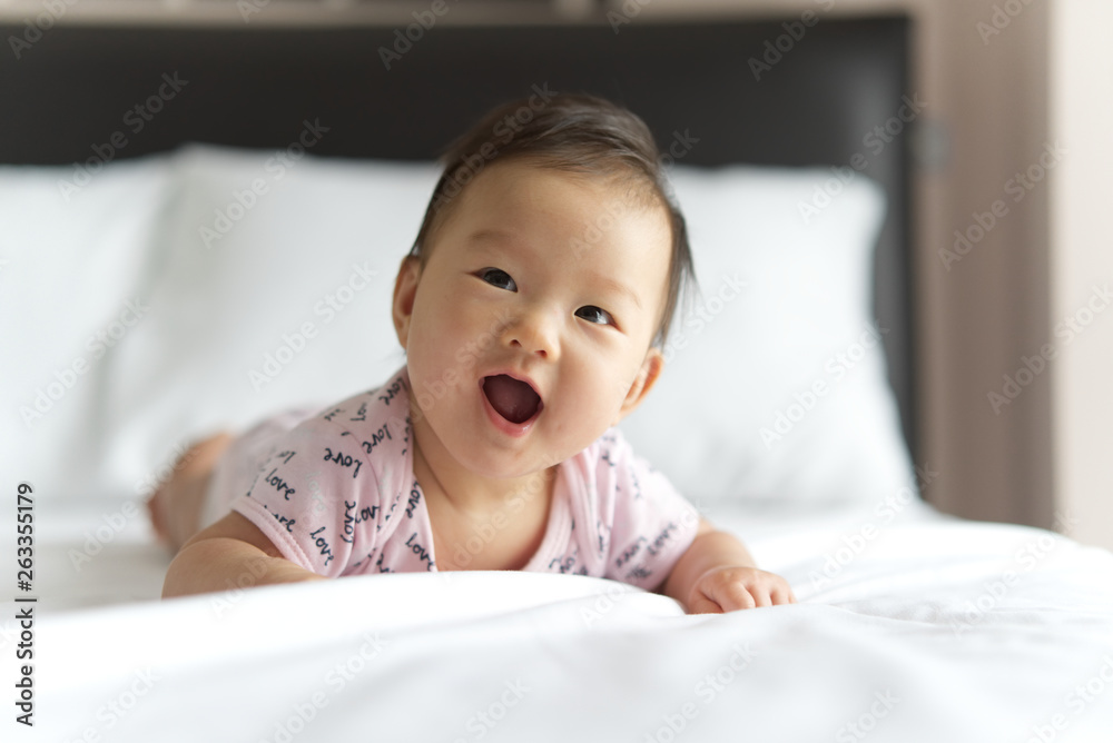 Young cute Asian baby crawling on bed in bedroom. The baby is smiling and looking at the right with 