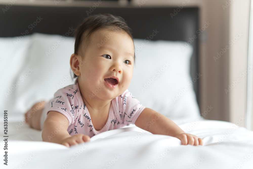 Young cute Asian baby crawling on bed in bedroom. The baby is smiling and looking at the left with h