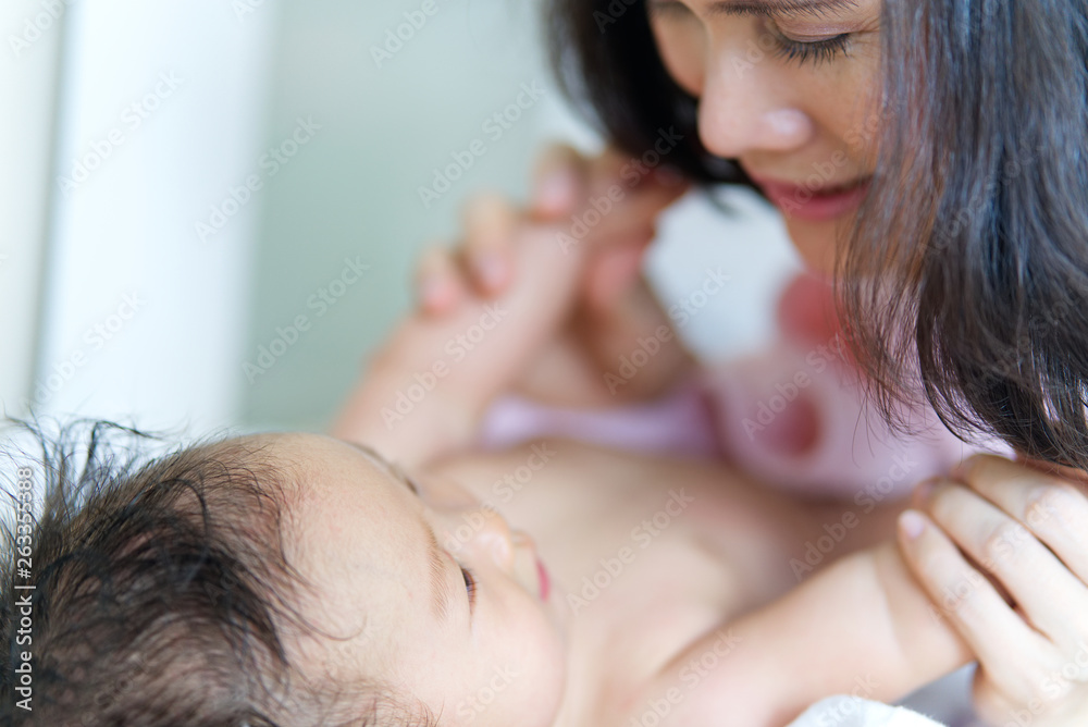 亚洲妈妈洗完澡后在换尿布的垫子上和孩子玩耍。她抱着两个孩子。