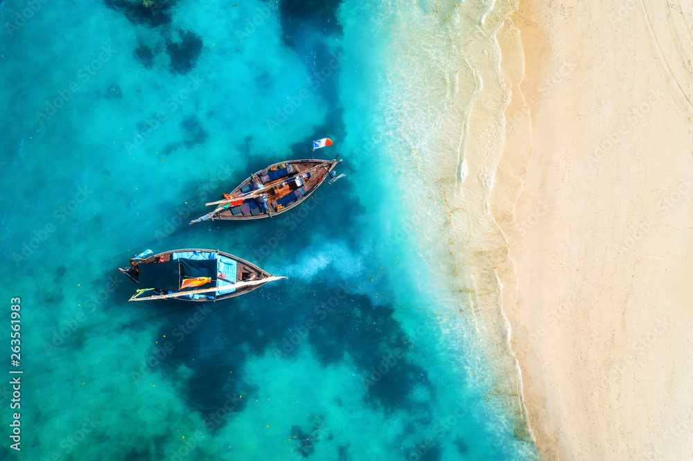 Aerial view of the fishing boats in clear blue water at sunset in summer. Top view from drone of boa