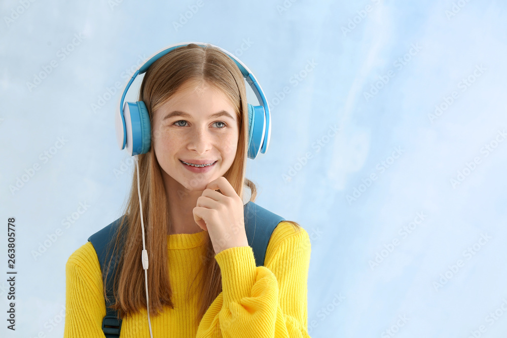 Cute teenage girl with headphones on color background