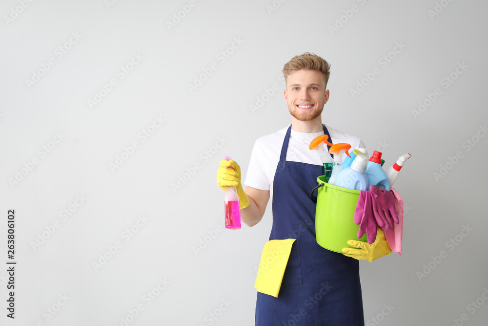 Portrait of male janitor with cleaning supplies on light background