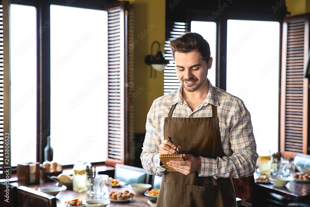 Young male waiter with notebook in restaurant