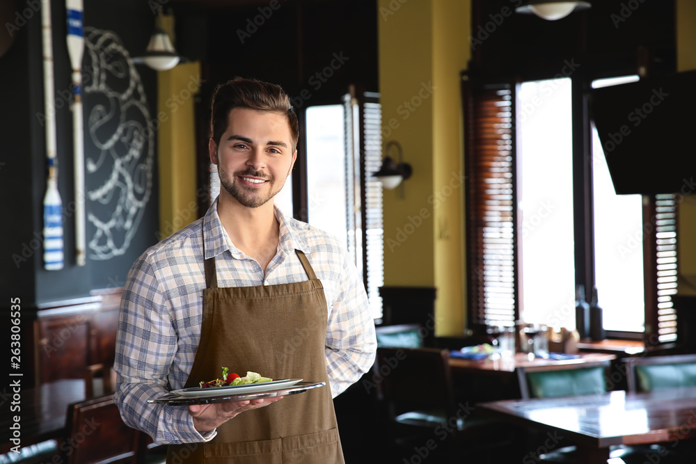 Young male waiter with salad in restaurant