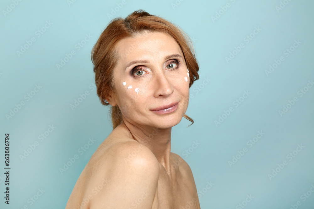 Mature woman with cream on her face against color background