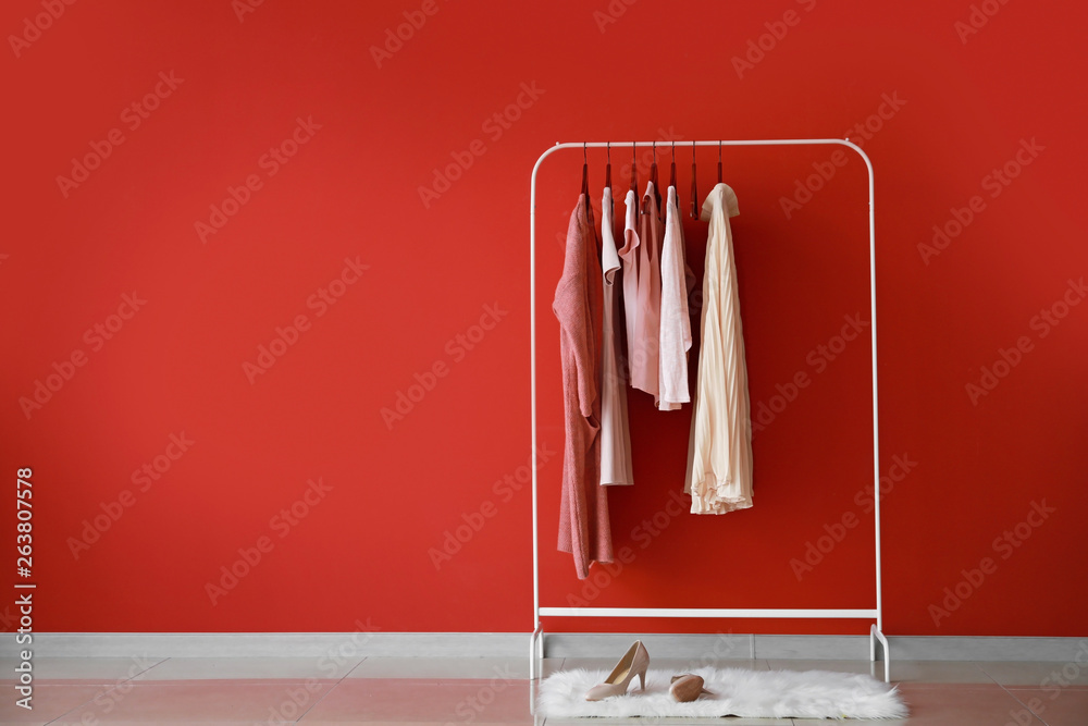 Rack with stylish clothes near color wall