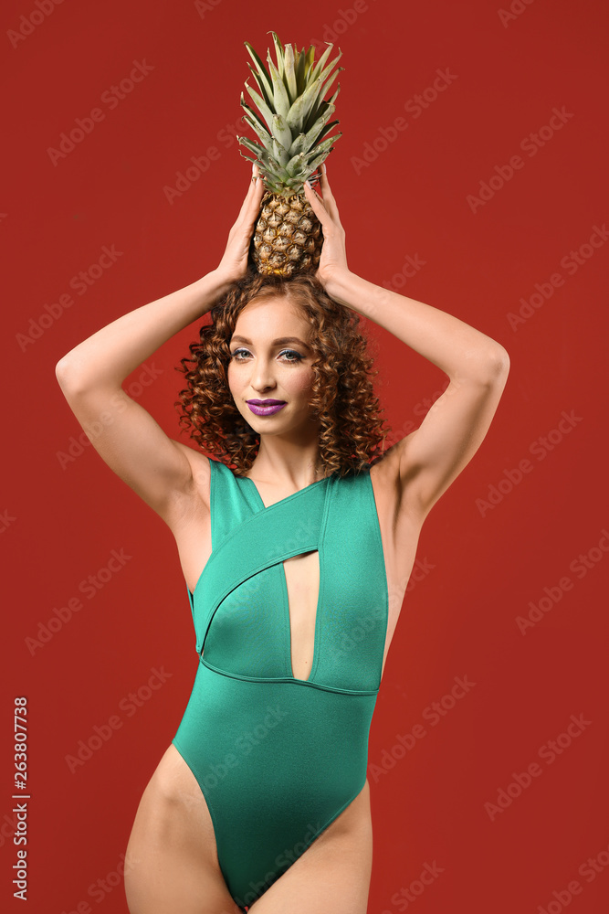 Beautiful young woman in swimsuit and with tasty pineapple on color background