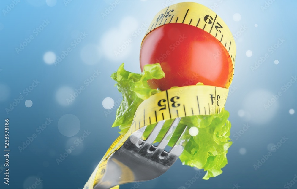 Fresh raw vegetables on fork and measuring tape on background