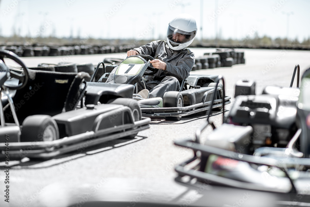 Racer in sportswear and protective helmet driving go-kart on the track