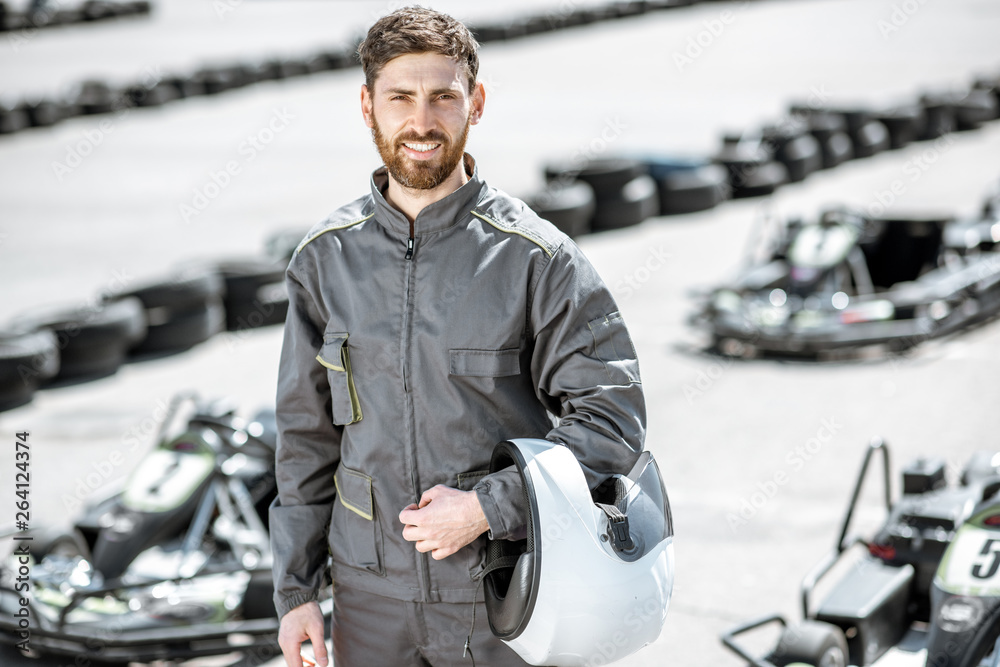 Portrait of a happy and excited racer in sportswear standing on the track with go-karts outdoors