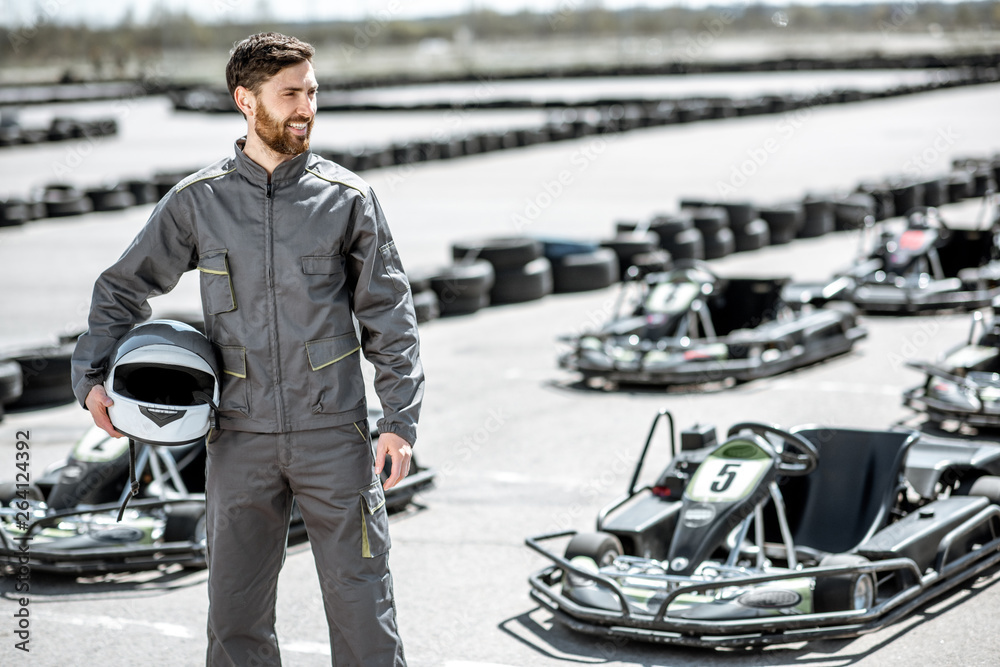 Portrait of a happy and excited racer in sportswear standing on the track with go-karts outdoors