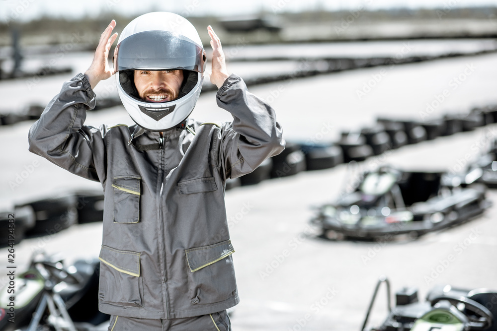 Portrait of a happy male racer in uniform wearing protective helmet while standing on the track with