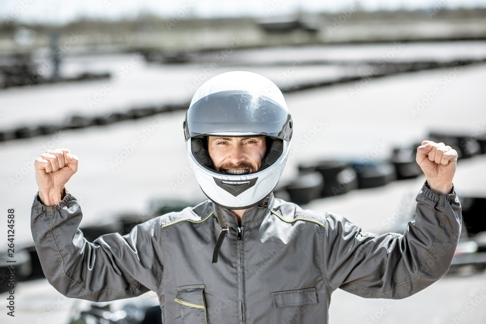 Portrait of a happy racer in protective sportswear standing as a winner of a go-kart race outdoors