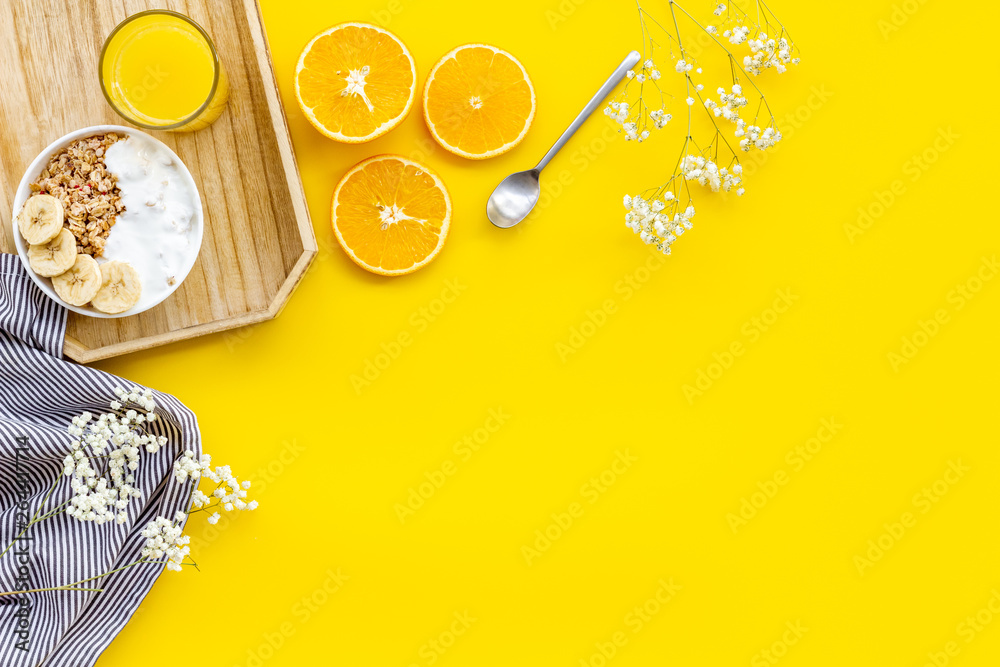 granola with banana slices and orange juice for breakfast on yellow background top view copyspace