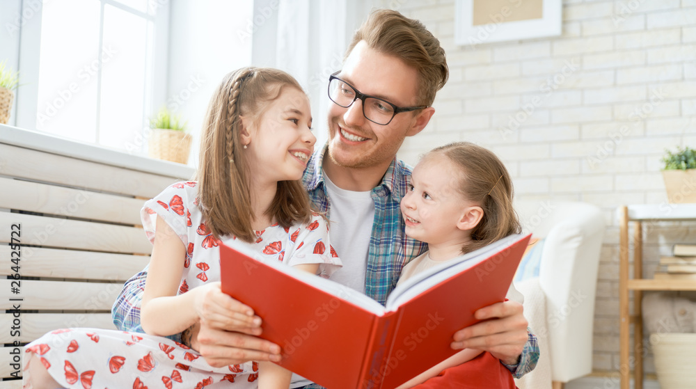 father reading a book to his daughters